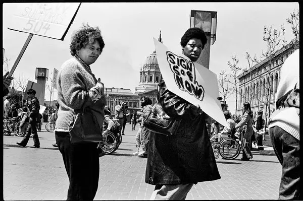 Demonstrators march on the street and are holding a sign. These demonstrators are protesting for section 504 of the rehabilitation act.