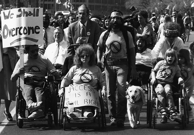 Activists with signs protest on the streets, and one activist has a guide dog.