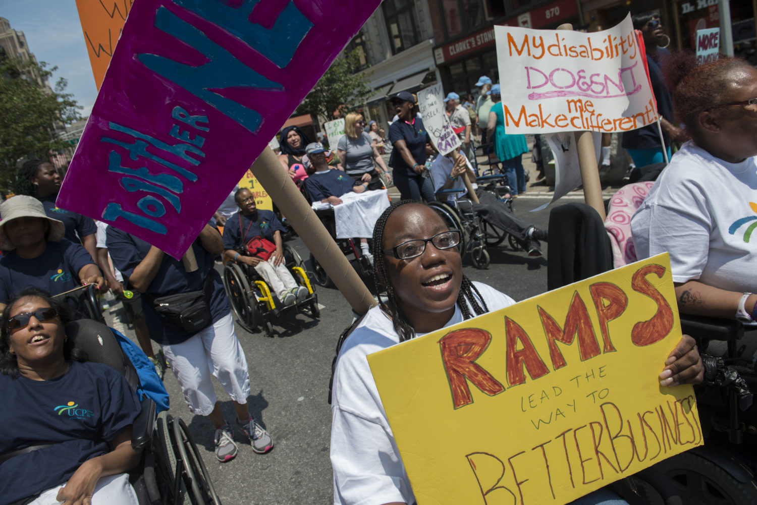 Disability rights protesters attend the first annual disability pride parade holding signs. They roll in their wheelchairs on the streets of New York City.